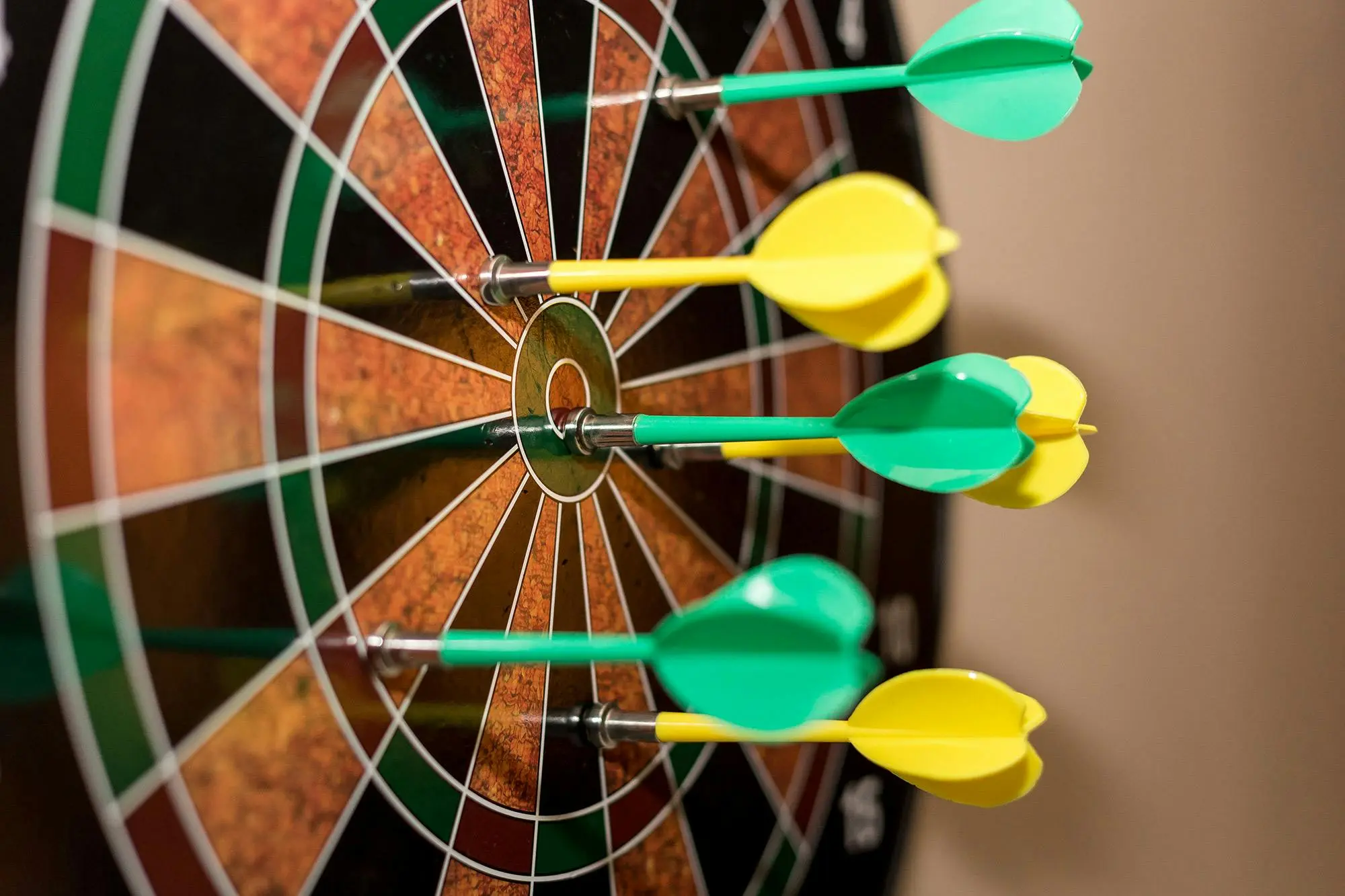 Six green and yellow darts in a dart board